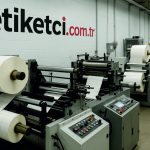 Baskısız rulo etiket üretiminin yapıldığı modern bir üretim tesisinde, etiket kesim ve sarım makineleriyle birlikte üretim süreci detaylı şekilde görülüyor. Arka planda "etiketci.com.tr" logosu duvarda yer alıyor.